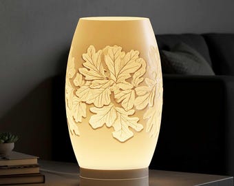 May include: Cream-colored, oval-shaped table lamp with a detailed leaf design. The lamp has a warm, glowing light emanating from within, and sits on a neutral-toned base. The leaves are raised and textured, adding depth to the design.