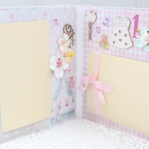 May include: A pink and white scrapbook with two blank pages. The pages are decorated with flowers, a dress, balloons, and the number "1".