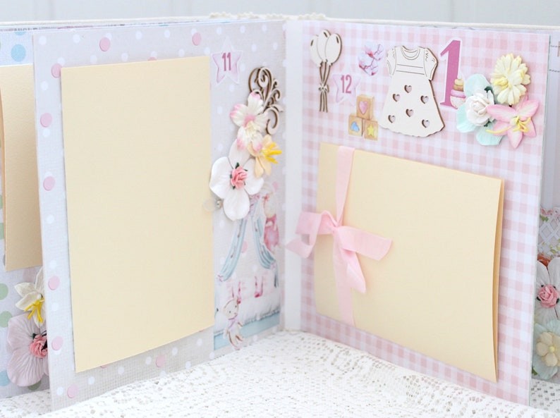 May include: A pink and white scrapbook with two blank pages. The pages are decorated with flowers, a dress, balloons, and the number "1".