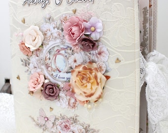 May include: A cream-coloured scrapbook with a textured cover featuring the text Always & Forever. The cover is decorated with layered paper flowers in shades of pink, peach, and white, small gold heart accents, and a white lace ribbon tie.