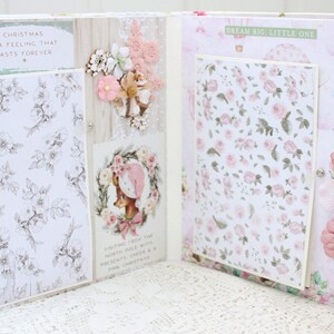 May include: Open scrapbook with a pink and white floral design. The left page has a white background with a black and white floral pattern and the text "Christmas is a feeling that lasts forever". The right page has a pink background with a white floral pattern and the text "Dream big, little one".