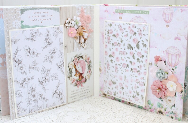 May include: Open scrapbook with a pink and white floral design. The left page has a white background with a black and white floral pattern and the text "Christmas is a feeling that lasts forever". The right page has a pink background with a white floral pattern and the text "Dream big, little one".