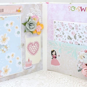 May include: A scrapbook with a light blue and white floral pattern on the left page and a pink and white floral pattern on the right page. The left page has a sticker that says "Hello" and the right page has a sticker that says "so sweet".