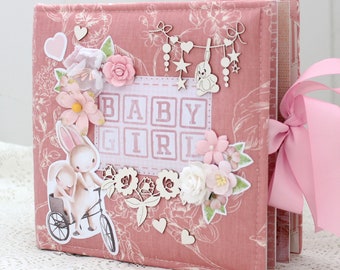 May include: Pink fabric baby scrapbook with a pink ribbon, a floral design, and the words "BABY GIRL" on the front.