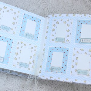 May include: A baby photo album with blue and white pages featuring a star pattern. The album has 12 photo slots with numbers 1 through 12 and the word "month" printed on each slot. The album is open to show the first six photo slots.