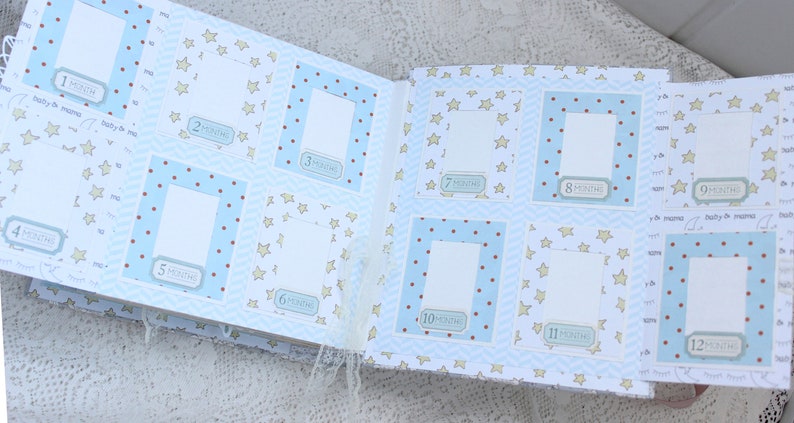 May include: A baby photo album with blue and white pages featuring a star pattern. The album has 12 photo slots with numbers 1 through 12 and the word "month" printed on each slot. The album is open to show the first six photo slots.