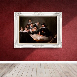 May include: A framed oil painting depicting a group of men gathered around a table, observing a dissected body. The painting is set in a dimly lit room with a dark background. The men are dressed in 17th-century attire, and the scene is reminiscent of a medical lecture.