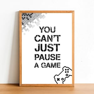 May include: A framed print with a black and white design. The print says "You can't just pause a game" and features a stylized image of a video game controller.