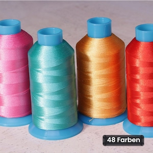 Op de afbeelding: Vier klossen glanzend borduurgaren in roze, talingblauw, goud en rood, elk voorzien van een lichtblauwe kunststof voet en dop. Een klein zwart rechthoekig label rechtsonder toont de witte tekst 48 Farben.