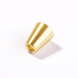 Könnte beinhalten: Eine kleine, kegelförmige Perle mit einer glatten, goldfarbenen Metalloberfläche. Das Objekt verfügt über eine hohle Öffnung am schmaleren Ende und eine polierte Oberfläche, die das Licht auf dem konisch zulaufenden, abgerundeten Körper reflektiert.