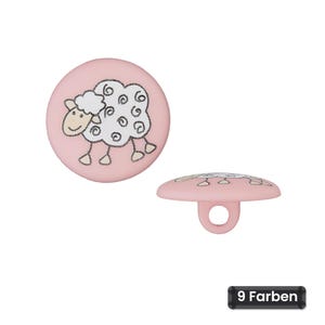 Op de afbeelding: Een ronde, lichtroze knoop met een grafische illustratie van een wit schaap met zwarte omlijningen. De knoop wordt getoond in bovenaanzicht en zijaanzicht, waarbij een ronde lus aan de achterkant zichtbaar is. De tekst luidt 9 Farben.