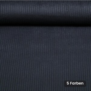 Peut inclure: Un tissu en velours côtelé bleu marine foncé présentant une texture distincte à côtes verticales. Le matériau est replié sur le dessus, créant un rouleau souple. Dans le coin inférieur droit, une petite étiquette noire affiche le texte 5 Farben.