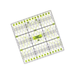 Peut inclure: Une règle de patchwork carrée en acrylique transparent mesurant 15 par 15 centimètres, avec des marquages de grille noirs et vert citron, des lignes d'angle de 30, 45 et 60 degrés, et le texte Snaply Quilting Ruler 15x15cm imprimé au centre.
