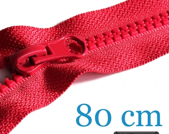 May include: A bright red plastic zipper with a matching red pull tab. The zipper tape has a woven texture and the teeth are thick and molded. The text 80 cm is printed in blue, and a black rectangular label displays the text 38 Farben.