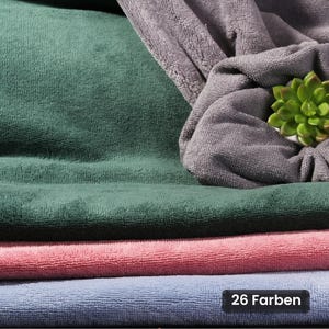 Könnte beinhalten: Ein Stapel gefalteter Mikrofasertücher in Dunkelgrün, Altrosa und Hellblau, mit einem darüber drapierten grauen Tuch. Eine kleine grüne Sukkulente liegt auf dem grauen Tuch. Ein schwarzes rechteckiges Etikett zeigt den Text 26 Farben.