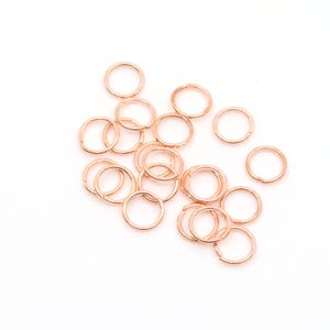 Könnte beinhalten: Eine Ansammlung kleiner, kreisförmiger Biegeringe in Roségold, die über den Rahmen verstreut sind. Jeder einzelne Ring besteht aus einem dünnen Metalldraht mit einer sichtbaren Nahtstelle, an der die Enden aufeinandertreffen.