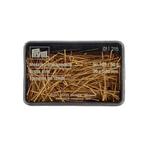 Op de afbeelding: Een rechthoekige, doorzichtige plastic doos gevuld met goudkleurige messing spelden. Het deksel bevat het Prym-logo, de tekst Messing Stecknadeln, Brass pins, Epingles en laiton, No. 105, 50 g, 30 x 0,80 mm, 011 215, Prym 52220 Stolberg Germany en www.prym-consumer.com.