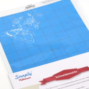 Può includere: Un tappetino da taglio blu con una stampa grafica bianca di farfalle e fiori. Il tappetino presenta una griglia nera con segni in pollici lungo i bordi. Il marchio Snaply Nähkram è stampato sul tappetino e sulla confezione, che mostra anche il testo Schneidematte e 20 x 30 cm.