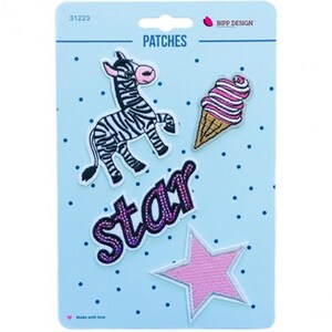 Könnte beinhalten: Ein Set aus vier bestickten Aufnähern auf einer hellblauen Karte mit dunkelblauen Punkten. Die Aufnäher zeigen ein schwarz-weißes Zebra, eine rosa-weiße Eiswaffel, das Wort star in violettem Glitzer und einen einfarbigen rosa Stern.