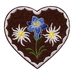 Könnte beinhalten: Ein herzförmiger Stickaufnäher mit dunkelbrauner Filzbasis und weißem, gewelltem Rand. In der Mitte befindet sich ein blauer Enzian mit gelber Mitte, flankiert von zwei weißen Edelweißblüten mit gelben Zentren und grünen Stielen.