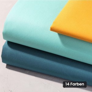 Peut inclure: Trois pièces de tissu pliées empilées les unes sur les autres dans des tons bleu sarcelle, turquoise clair et jaune vif. Le tissu présente une texture tissée visible. Une petite étiquette rectangulaire noire affiche le texte 14 Farben.