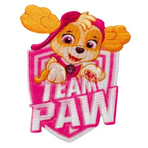 Pode incluir: Um emblema bordado com um personagem de cão de desenho animado com pelo castanho e grandes orelhas cor de laranja a usar um gorro cor-de-rosa. A personagem está sobre o texto branco "TEAM PAW" num fundo cor-de-rosa em forma de escudo.