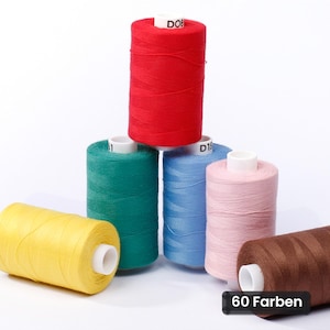 Op de afbeelding: Een verzameling van zes cilindrische klossen naaigaren in rood, groen, blauw, roze, geel en bruin. De klossen hebben witte plastic kernen met zichtbare tekstlabels, waaronder D08, D16 en een zwart rechthoekig label met de tekst 60 Farben.