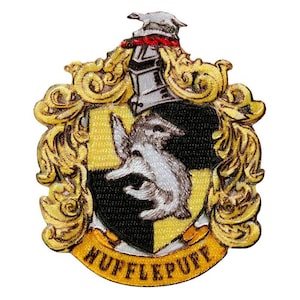 Pode incluir: Um emblema bordado apresentando o brasão de Hufflepuff com um escudo preto e amarelo, um emblema central de texugo, um elmo prateado no topo e ornamentos dourados ao redor do escudo com a palavra HUFFLEPUFF em uma faixa.