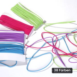 Op de afbeelding: Vier spoelen elastisch koord in limoengroen, felroze, paars en lichtblauw, met losse draden van dezelfde kleuren die rechts in de knoop zitten. Een klein zwart rechthoekig label in de rechterbenedenhoek toont de tekst 38 Farben.