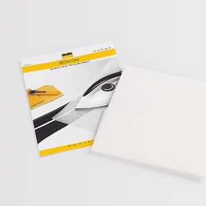 Könnte beinhalten: Ein weißes Bügelvlies in einer Verpackung mit Vlieseline-Logo. Die Verpackung zeigt einen gelben Streifen mit dem Text IRON ON, eine Abbildung eines Bügeleisens und Stoffmuster. Das Produkt selbst ist ein quadratisches, halbtransparentes weißes Textil.
