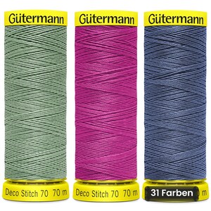 Może przedstawiać: Trzy szpulki nici Gütermann Deco Stitch 70 w kolorach szałwiowej zieleni, magenty i łupkowego błękitu. Każda szpulka ma żółte końcówki z napisem Gütermann, Deco Stitch 70 i 70 m. Trzecia szpulka zawiera napis 31 Farben.
