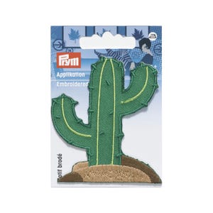 Pode incluir: Um emblema bordado de cacto em verde com linhas verticais verde-claras e pequenos detalhes de pontos verde-escuros, sobre uma base bege e castanha, apresentado numa embalagem da marca Prym com detalhes em azul.