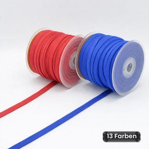Könnte beinhalten: Zwei Kunststoffspulen mit flachem Stoffband, eine in leuchtendem Rot und eine in leuchtendem Blau, die jeweils ein Stück Material abwickeln. Der Text 13 Farben ist in der unteren rechten Ecke des Bildes zu sehen und zeigt die Farbvielfalt.