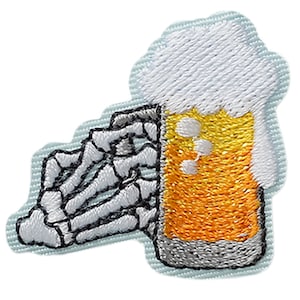 Puede incluir: Un parche bordado que muestra una mano esquelética agarrando un vaso de cerveza dorada con una espesa espuma blanca. El diseño utiliza hilo amarillo, blanco y gris sobre una base de tela azul claro con un borde cortado siguiendo la forma.