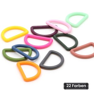 Könnte beinhalten: Eine Sammlung von D-Ringen in verschiedenen Farben, darunter Gelb, Pink, Lila, Grün, Blau, Orange und Grau. Die Beschlagteile sind im Bild verstreut und ein kleines schwarzes rechteckiges Etikett zeigt den Text 22 Farben.
