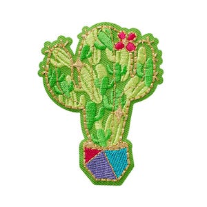Puede incluir: Un parche bordado con forma de cactus en una maceta. El cactus está representado en varios tonos de verde con contornos de hilo dorado y una pequeña flor rosa. La maceta presenta secciones geométricas en rojo, morado y azul con bordes dorados.