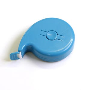 Può includere: Un metro a nastro retrattile blu brillante con un involucro in plastica liscio, arrotondato e a forma di goccia. Il dispositivo è dotato di un pulsante circolare centrale per ritrarre il nastro e di una piccola linguetta all'apertura.