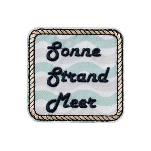 Pode incluir: Um emblema quadrado bordado com um padrão de ondas em azul claro e branco. O texto "Sonne Strand Meer" está bordado com fio azul-marinho escuro no centro. A borda é finalizada com um bordado estilo corda em bege e castanho escuro.