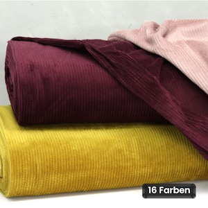 Könnte beinhalten: Drei Rollen Cordstoff, die übereinander gestapelt sind, in den Farben Dunkelburgunder, Senfgelb und zartem Altrosa. Der Stoff weist eine ausgeprägte vertikale Rippenstruktur auf, und ein kleines schwarzes Etikett zeigt den Text 16 Farben.