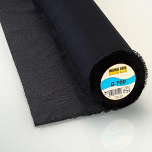 Peut inclure: Un rouleau de tissu thermocollant noir Vlieseline G 700. L'étiquette circulaire à l'extrémité du rouleau affiche le nom de la marque, le numéro de modèle G 700, un code-barres et les dimensions de 90 cm par 25 m, avec 100% CO imprimé en dessous.