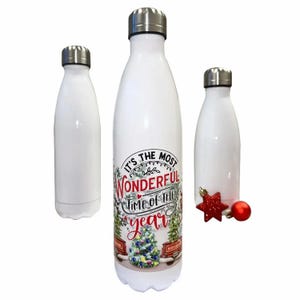 Op de afbeelding: Drie witte metalen waterflessen met zilveren doppen. De middelste fles heeft een feestelijke afbeelding met de tekst 'IT'S THE MOST WONDERFUL TIME OF THE YEAR' boven een versierde kerstboom. Een kleine rode ster ligt bij de rechterfles.