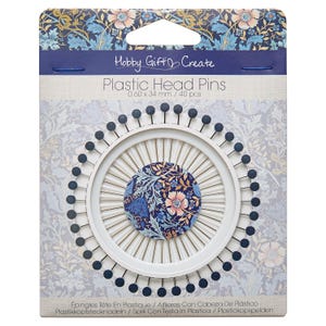 Könnte beinhalten: Eine Packung mit 40 Hobby Gift Create Plastikkopfstecknadeln in der Größe 0,60 x 34 mm. Die Nadeln haben dunkelblaue, runde Köpfe und sind in einem kreisförmigen weißen Kunststoffhalter mit einem floralen Mittelstück angeordnet.