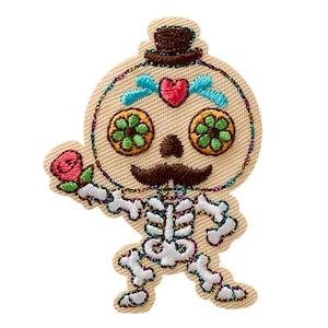Pode incluir: Um emblema bordado apresentando um esqueleto com bigode e cartola castanhos. O crânio tem olhos de flores verdes, um detalhe de coração vermelho na testa e detalhes azuis. O esqueleto segura uma rosa cor-de-rosa e tem ossos brancos.