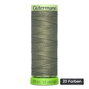 Op de afbeelding: Een klos olijfgroen naaigaren van Gütermann. De klos heeft een lichtgroene boven- en onderkant. Op de onderkant staat de tekst 30 m - 33 yds/vgs. Een apart zwart rechthoekig label naast de klos toont de tekst 20 Farben in het wit.