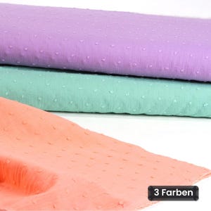 Puede incluir: Tres piezas de tela dobladas en lavanda, verde menta y melocotón, cada una con un patrón de puntos suizos texturizado en la superficie. Una pequeña etiqueta rectangular negra en la esquina inferior derecha muestra el texto blanco 3 Farben.