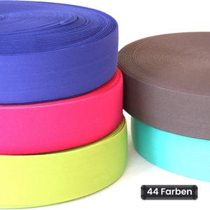 Op de afbeelding: Een stapel van vier ronde spoelen met elastisch lint in levendige kleuren, waaronder koningsblauw, felroze, limoengroen, bruin en turquoise. Een klein zwart rechthoekig label in de rechterbenedenhoek toont de tekst 44 Farben.