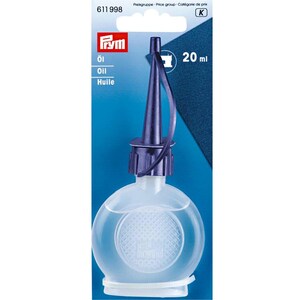 May include: A 20 ml bottle of Prym sewing machine oil in a clear, round plastic container with a dark blue pointed applicator nozzle and cap. The product is mounted on a blue and white cardboard backing card featuring the Prym logo and text.