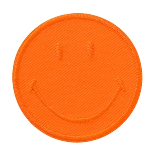 Könnte beinhalten: Ein kreisförmiger, orangefarbener Aufnäher mit einem gestickten Smiley-Gesicht. Der Aufnäher hat einen einfarbigen orangefarbenen Hintergrund mit zwei vertikalen, ovalen Augen und einem geschwungenen Mund, die in einem etwas dunkleren Orangeton gestickt sind.