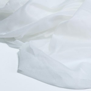 Pode incluir: Um tecido branco leve e transparente com uma trama fina e semitransparente. O material está drapeado em dobras suaves e fluidas, criando sombras e reflexos subtis na superfície, enfatizando a sua textura delicada, arejada e translúcida.