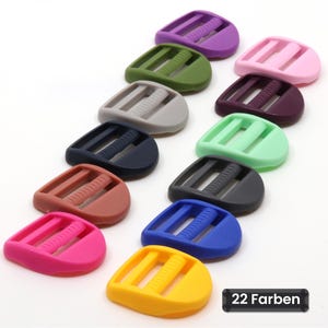 Puede incluir: Una colección de doce hebillas deslizantes de plástico dispuestas en dos filas, con una variedad de colores sólidos que incluyen amarillo, azul, rosa, negro, verde, morado y marrón. Una etiqueta rectangular negra muestra el texto 22 Farben.